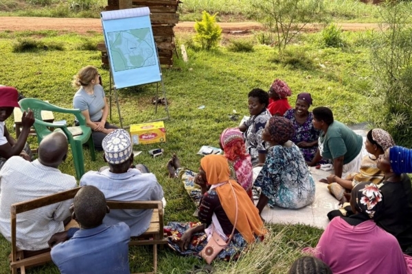 An intern sitting on the ground next to an easel presenting a map to a group of people.